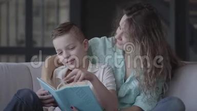 一位美丽的年轻母亲给坐在沙发上的漂亮儿子读一本书的肖像。 兄弟情谊。 家庭